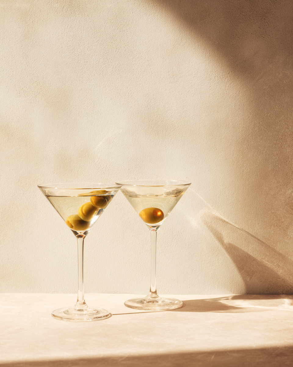 Ljus fotografisk poster med två torra martinis och långa skuggor på varm kalkfärgad vägg.
